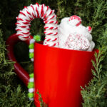Ornament in the shape of a cup of hot cocoa with whipped cream and a candy cane.